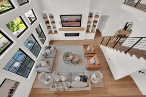 Living room with wood finished floors, a fireplace, built in shelves, and a high ceiling