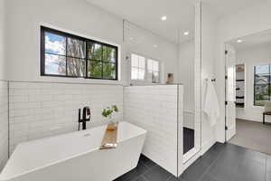 Master en suite and bathroom with walk in shower, tile walls, a freestanding tub, recessed lighting, and dark tile patterned floors