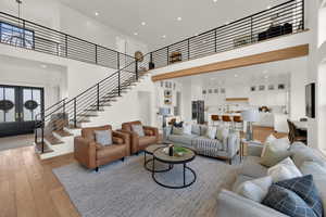 Living area featuring a high ceiling, recessed lighting, light wood-style floors, stairs, and french doors