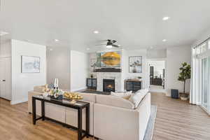 Living room featuring light wood-style floors, a stone fireplace, a ceiling fan, and recessed lighting