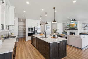 Kitchen featuring dark brown cabinets, an island with sink, light stone counters, hanging light fixtures, and appliances with stainless steel finishes