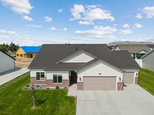 View of front of property featuring brick siding, a front yard, driveway, and roof with shingles