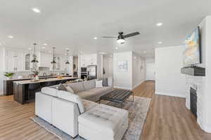 Living room with a stone fireplace, light wood-style floors, ceiling fan, and recessed lighting