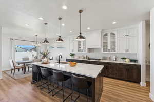 Kitchen with dark brown cabinets, tasteful backsplash, white cabinetry, a kitchen bar, and hanging light fixtures
