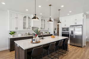 Kitchen with appliances with stainless steel finishes, light wood-style flooring, dark brown cabinetry, recessed lighting, and an island with sink
