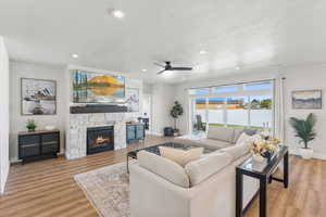 Living room featuring recessed lighting, a textured ceiling, a stone fireplace, a ceiling fan, and light wood-type flooring