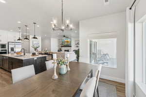 Dining space with a chandelier, a ceiling fan, a stone fireplace, light wood finished floors, and recessed lighting