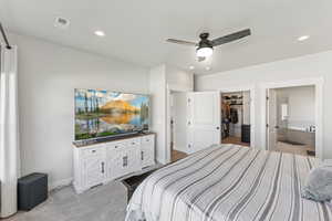 Bedroom with connected bathroom, light carpet, a ceiling fan, recessed lighting, and a walk in closet