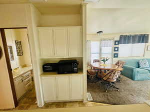 Kitchen with white cabinetry, black microwave, open floor plan, and light countertops