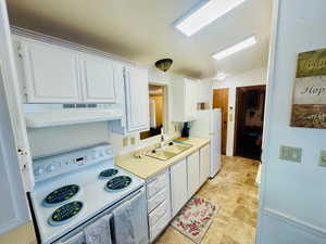 Kitchen featuring electric stove, white cabinetry, light countertops, under cabinet range hood, and vaulted ceiling