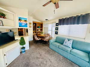 Carpeted living room featuring vaulted ceiling, ceiling fan, and built in shelves