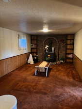 Living room featuring wainscoting, wood walls, built in features, a wood stove, and a textured ceiling