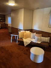 Living room featuring wood walls, wainscoting, a textured ceiling, and dark colored carpet