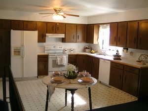 Kitchen with white appliances, light countertops, ceiling fan, under cabinet range hood, and brown cabinetry