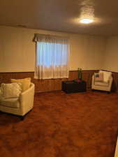 Carpeted living room with wooden walls, a wainscoted wall, and a textured ceiling