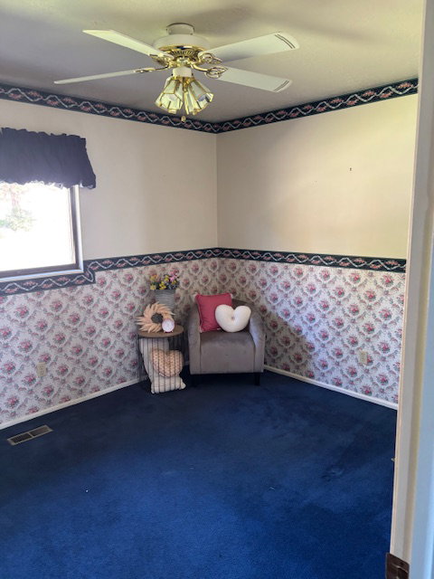 Sitting room featuring wallpapered walls, a ceiling fan, and dark colored carpet