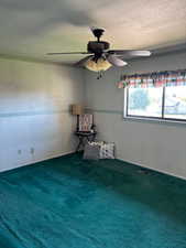 Spare room with a textured ceiling, dark colored carpet, and a ceiling fan