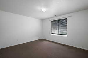 Empty room featuring a textured ceiling and dark carpet