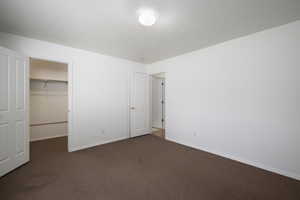 Unfurnished bedroom with a walk in closet, dark colored carpet, and a textured ceiling