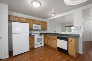 Kitchen with white appliances, a textured ceiling, dark wood-style flooring, dark countertops, and brown cabinets