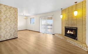 Unfurnished living room featuring a brick fireplace, wood finished floors, and a chandelier