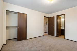 Unfurnished bedroom featuring light colored carpet, a closet, and ensuite bath