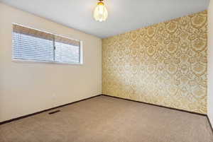 Spare room featuring wallpapered walls, carpet floors, and an accent wall