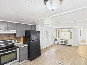 Kitchen featuring stainless steel range with electric cooktop, freestanding refrigerator, gray cabinets, light countertops, and under cabinet range hood