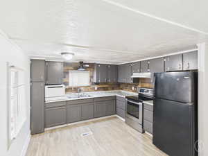 Kitchen with freestanding refrigerator, a textured ceiling, stainless steel range with electric stovetop, light countertops, and light wood-style flooring