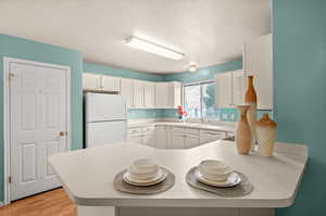 Kitchen featuring white appliances, a textured ceiling, white cabinetry, a peninsula, and light countertops