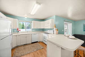 Kitchen featuring white appliances, a peninsula, light countertops, light wood-type flooring, and white cabinetry