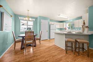 Kitchen with a kitchen breakfast bar, a chandelier, light countertops, freestanding refrigerator, and light wood-type flooring