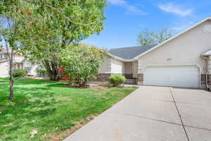View of front of property with stucco siding, a front lawn, a garage, concrete driveway, and stone siding