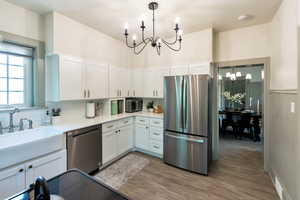 Kitchen featuring a chandelier, stainless steel appliances, white cabinetry, wood finished floors, and light stone counters