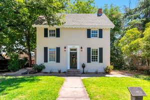 View of front facade featuring roof with shingles, a front lawn, a chimney, and stucco siding
