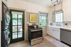 Kitchen with appliances with stainless steel finishes, white cabinetry, light wood-style flooring, and stacked washer / dryer