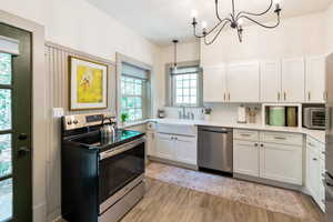 Kitchen with stainless steel appliances, white cabinetry, light wood-style floors, pendant lighting, and a chandelier