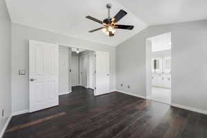 Unfurnished bedroom with dark wood-style flooring, vaulted ceiling, ceiling fan, and ensuite bath