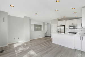 Kitchen with white cabinets, a peninsula, stainless steel appliances, backsplash, and open floor plan