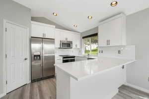Kitchen with appliances with stainless steel finishes, lofted ceiling, a peninsula, white cabinetry, and decorative backsplash