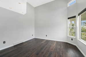 Empty room featuring a high ceiling and dark wood-type flooring
