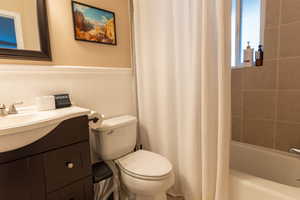 Full bath featuring vanity, shower / bath combo, and wainscoting