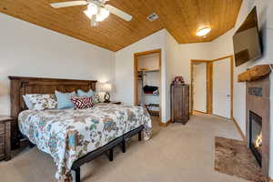 Bedroom with wood ceiling, light carpet, vaulted ceiling, a fireplace, and a closet