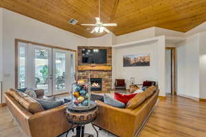 Living area featuring ceiling fan, a fireplace, wooden ceiling, high vaulted ceiling, and light wood-type flooring