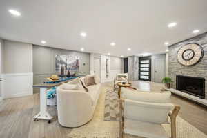 Living area featuring a decorative wall, a stone fireplace, light wood-style flooring, recessed lighting, and wainscoting