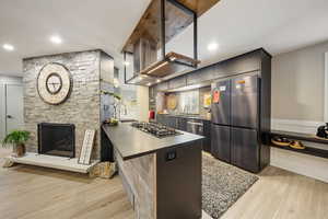 Kitchen with dark countertops, appliances with stainless steel finishes, light wood finished floors, tasteful backsplash, and a stone fireplace