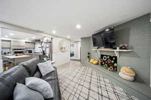 Living room featuring light wood finished floors, recessed lighting, brick wall, and a fireplace with raised hearth