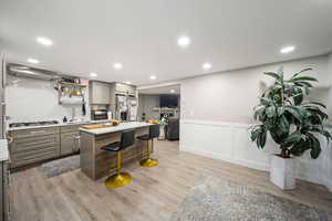 Kitchen with gray cabinetry, a breakfast bar, wainscoting, light wood finished floors, and appliances with stainless steel finishes