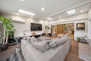 Living area featuring a wainscoted wall, a skylight, dark wood finished floors, a wall mounted AC, and recessed lighting