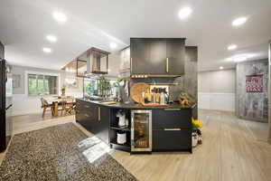 Bar area with modern cabinets, dark cabinets, light wood-style flooring, beverage cooler, and pendant lighting